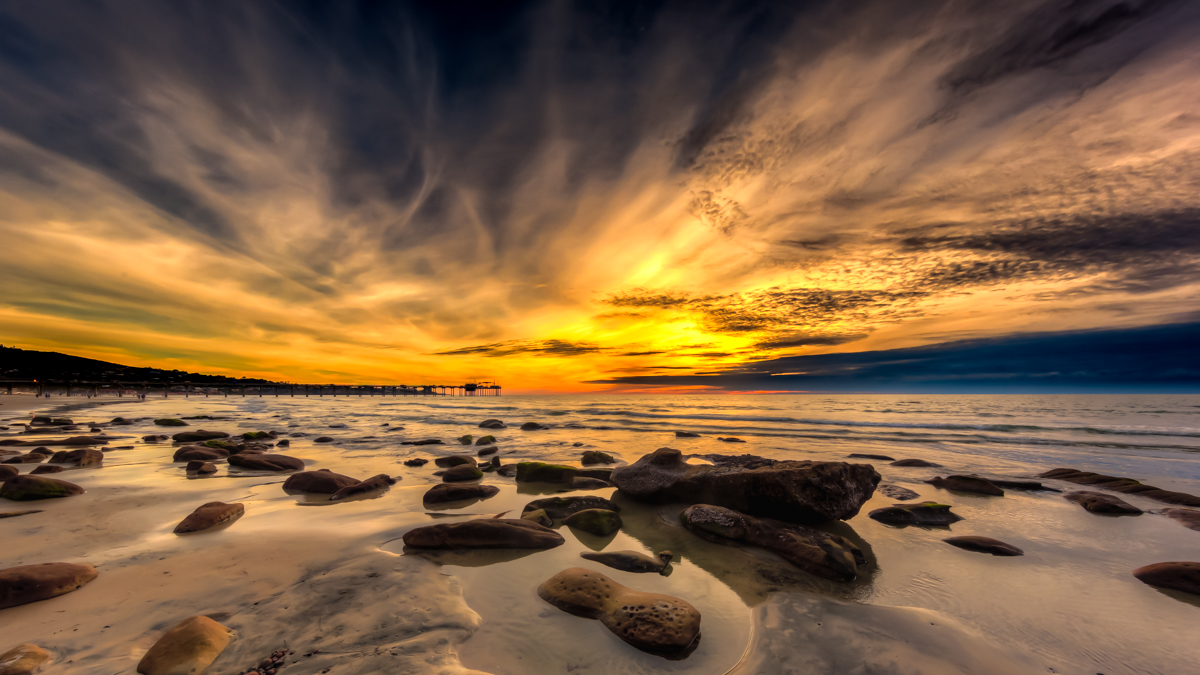 Dramatic sunset over San Diego coastline with rocks in the foreground — photographed by Arnel Garcia